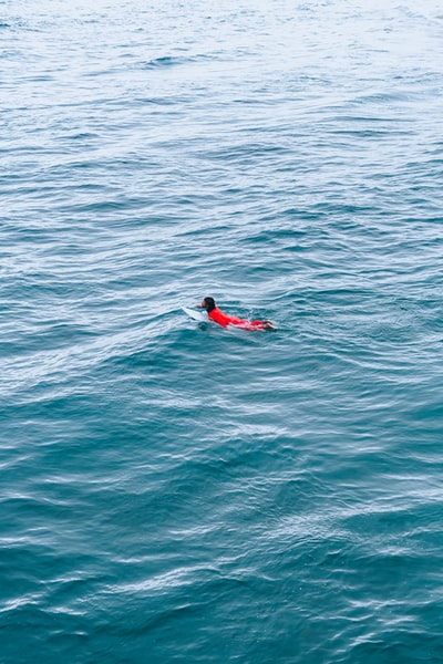 During the day, dressed in a red suit in blue sea surfing
